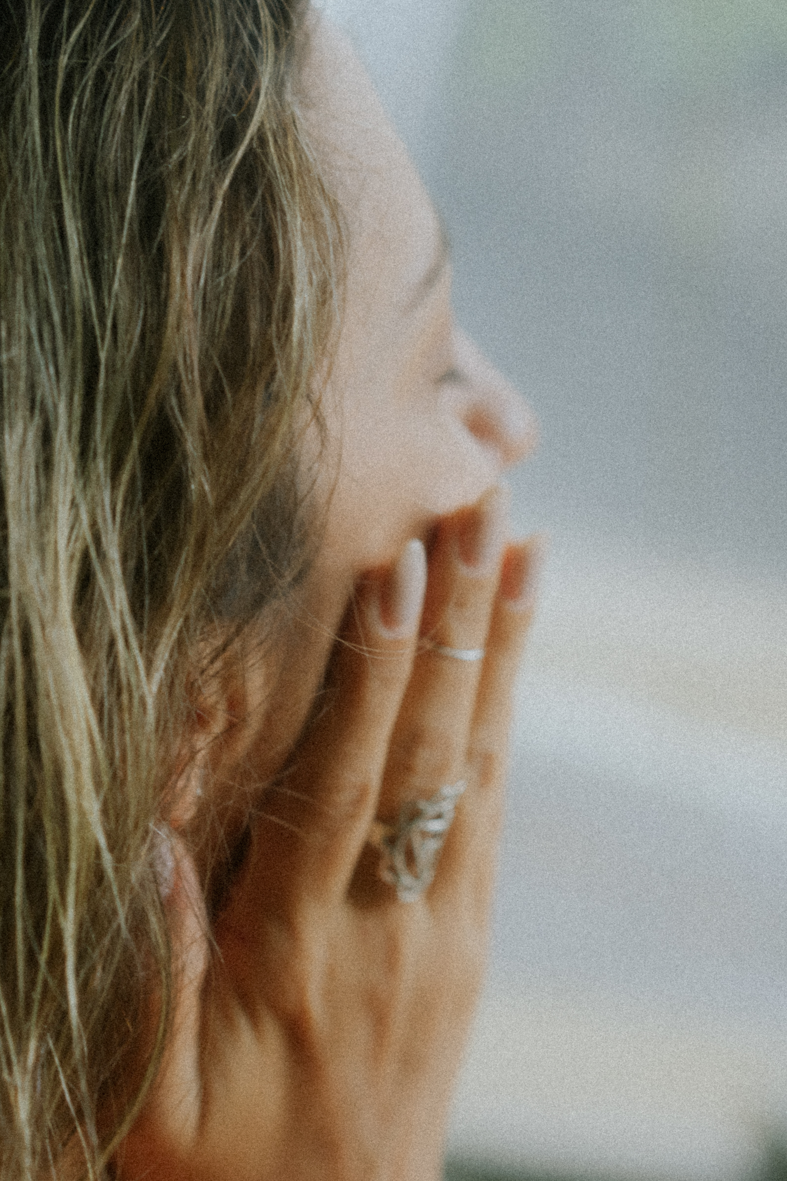 Woman touching her face gently while looking out a window, symbolizing concern or reflection about facial aging—ideal for articles about facelift alternatives or skin rejuvenation.