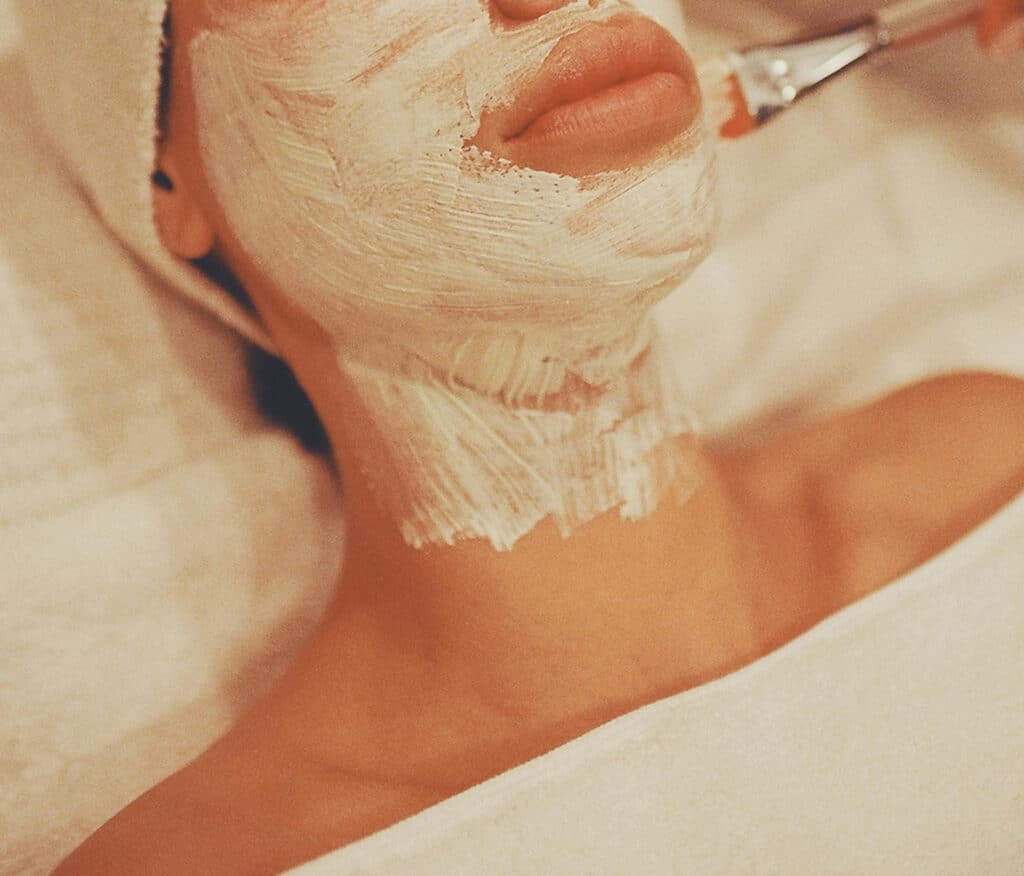 Esthetician applying a facial mask with a brush to a client's face and neck during a custom facial at Good Chemistry med spa in Cumming, GA